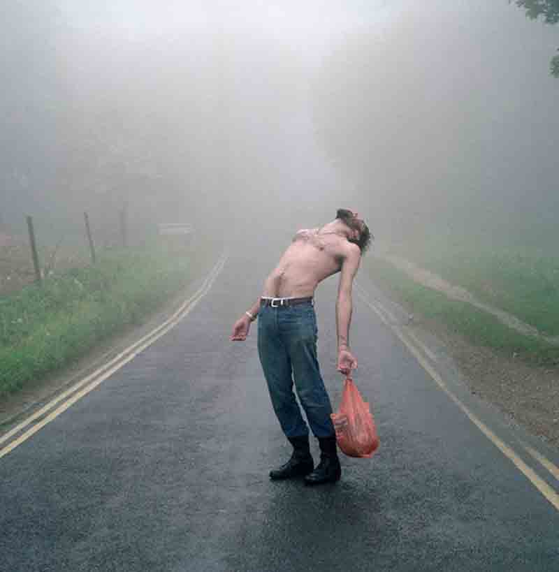 a slim shirtless man looking at the sky on a foggy day