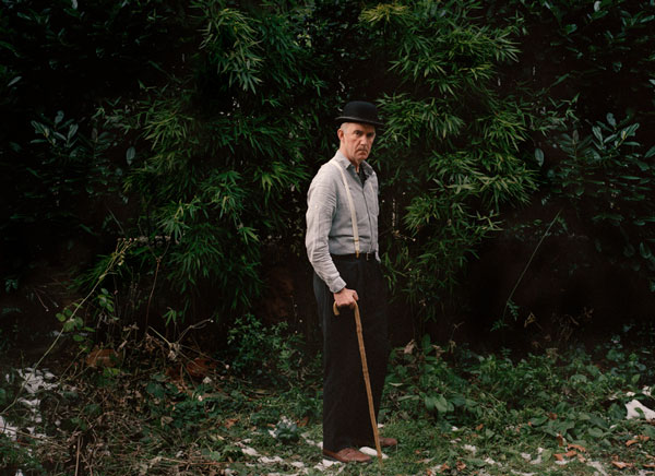 An image of a old man holding a cane and wearing formals.