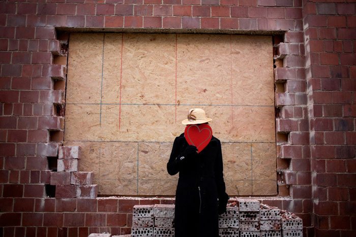 An image of man posing with a heart against a brick background