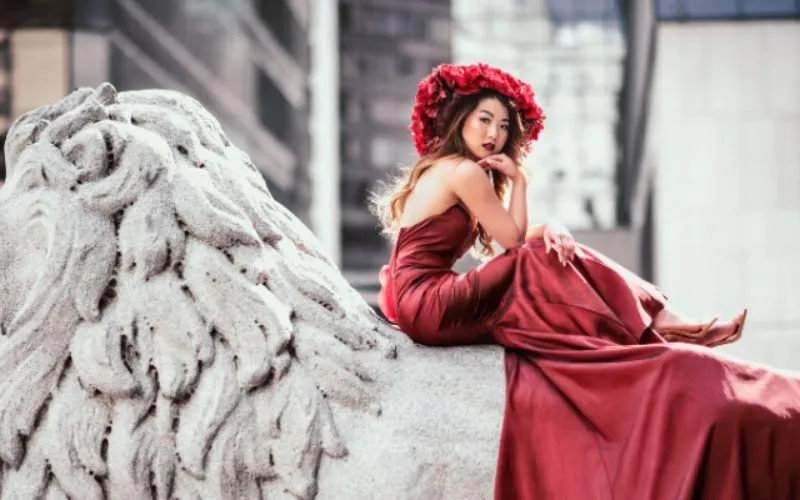 An image of a woman dressed in red posing on top of a statue lion