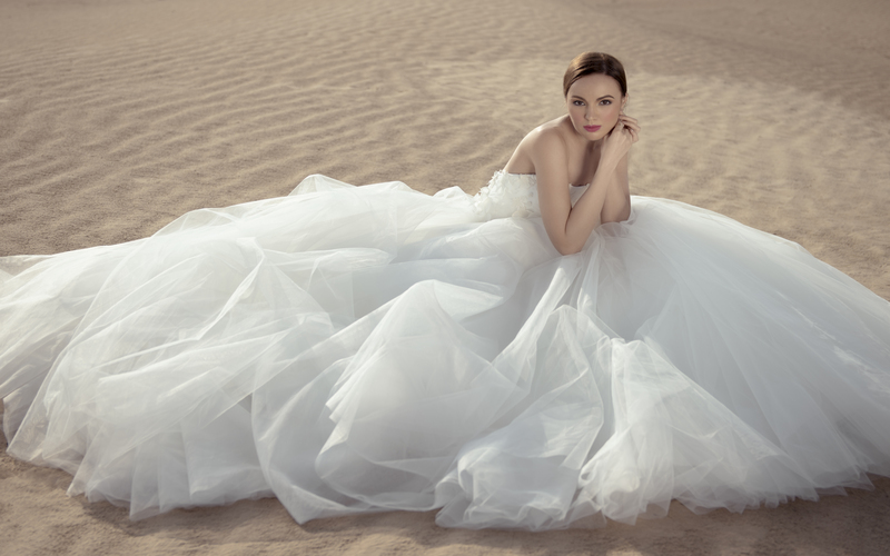 a model sitting on desert soil wearing white wedding gown
