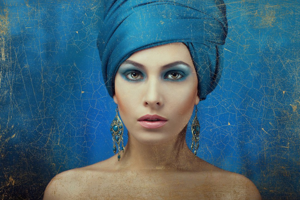 headshot of a model wearing a blue headwrap and blue eye makeup with a golden texture overlay