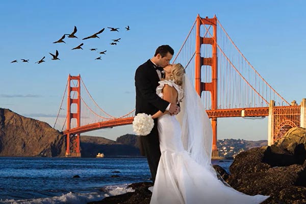 An image of a couple kissing in wedding dress against a background of bridge and birds