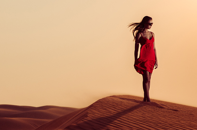 A model wearing red dress and posing in a desert