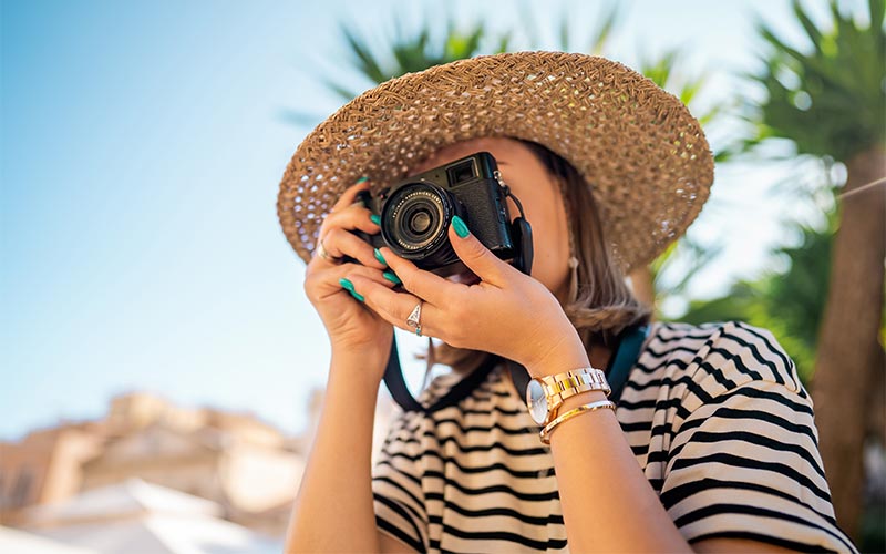 A woman wearing hat clicking picture with a camera