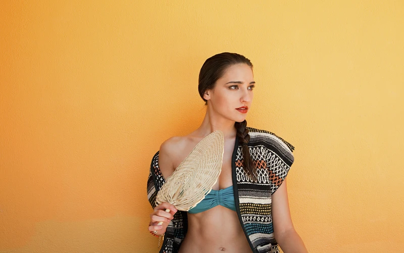 Woman in a patterned outfit photographed against a bold orange background