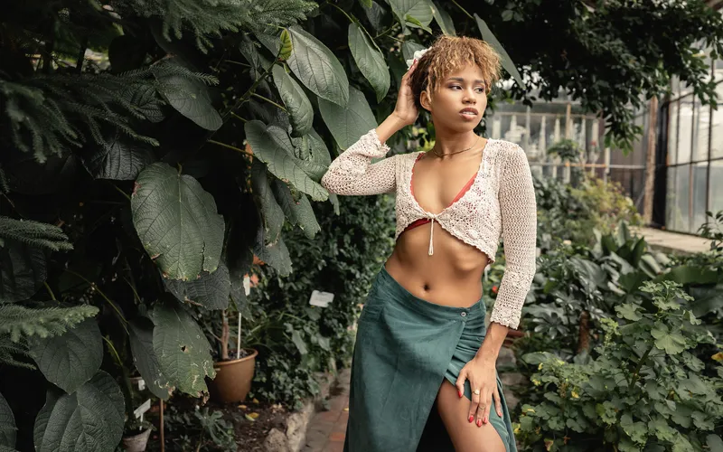 Woman in a cropped top and long skirt standing among green plants