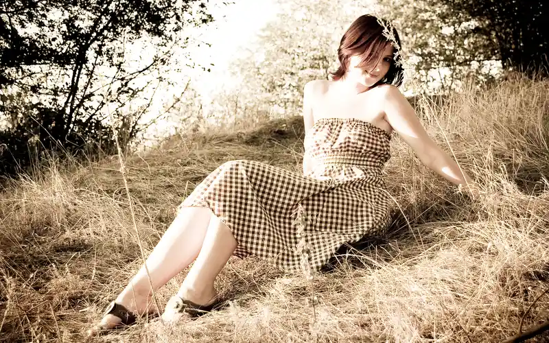 Woman in a checkered dress sitting in a dry grass field