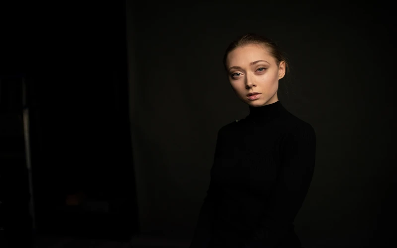 Woman in a black turtleneck photographed against a dark backdrop with dramatic lighting