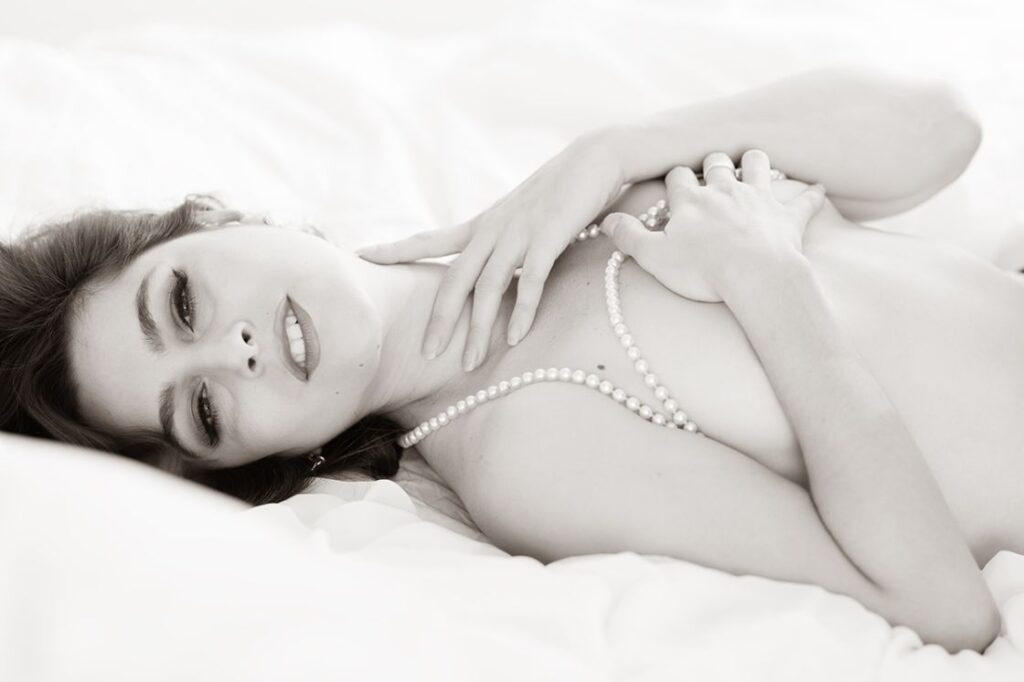 image by famous nude photographer-bw image of topless female model lying down, covering her chest and looking at the camera