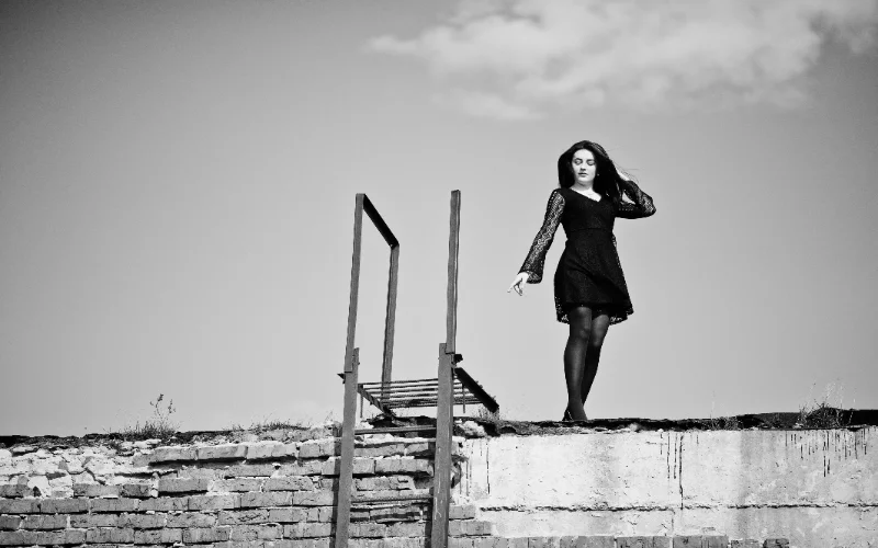 Black and white figure photography of a woman in a black dress standing on a rooftop ladder