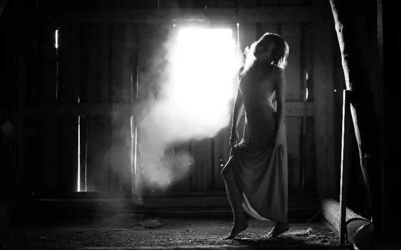 Silhouette of a woman in a flowing dress backlit by a window, black and white figure photography