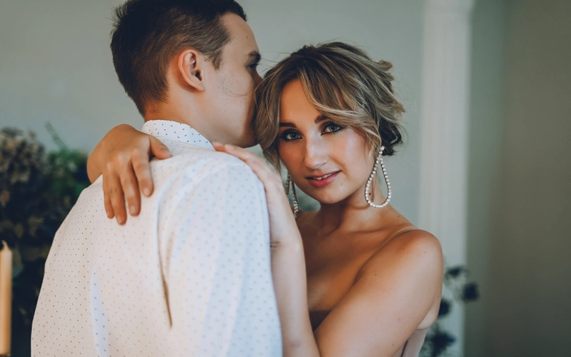 woman hugging a man in a white shirt while wearing large earrings and posing for boudoir wedding photography