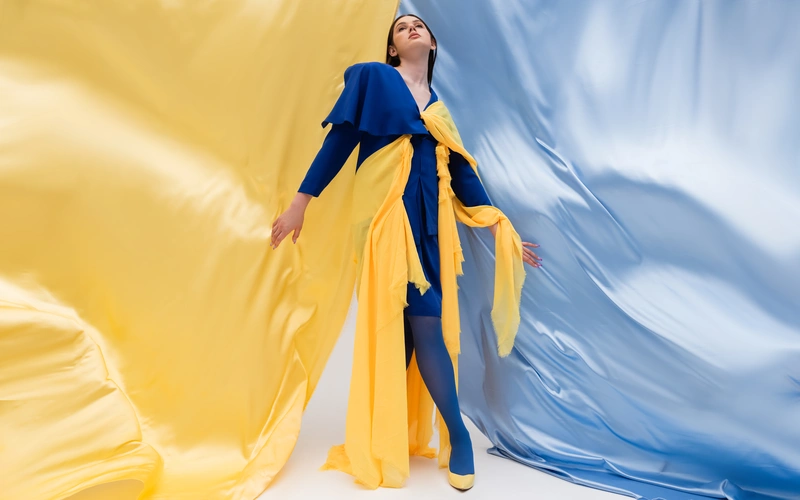 Woman in a blue and yellow gown with fabric flowing dramatically around her for an artistic glamour photography shoot
