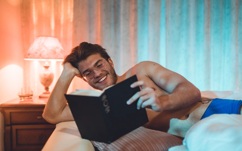 Candid boudoir portrait of a man in glasses reading a book