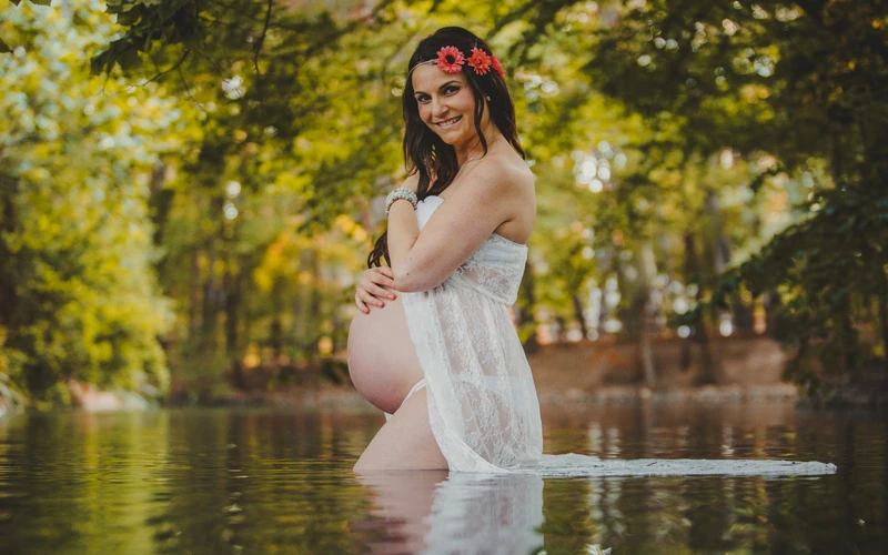 Boudoir maternity photo of a woman holding her belly in nature