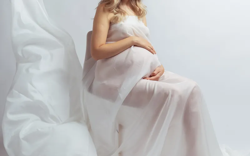 Boudoir pregnancy picture of a woman wrapped in a white curtain