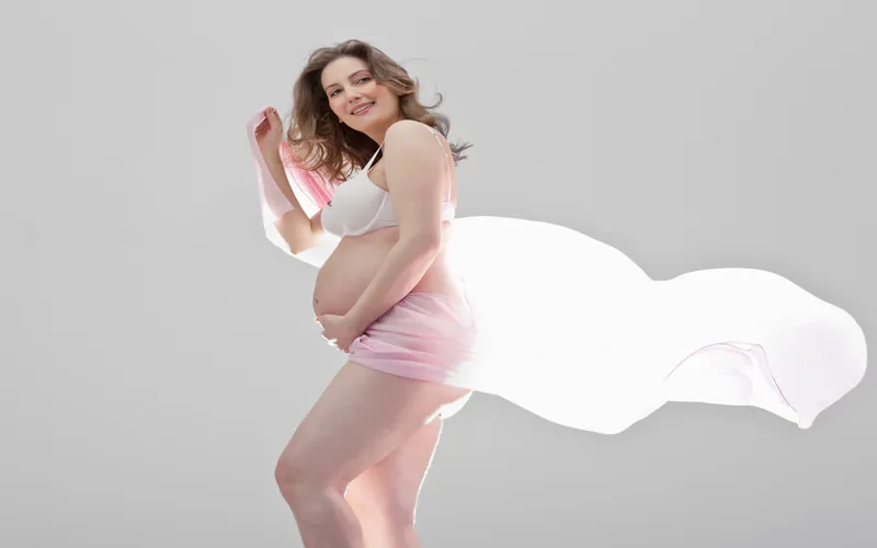 pregnant woman posing with a light pink fabric