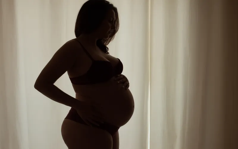 Silhouette of a pregnant woman standing against curtains