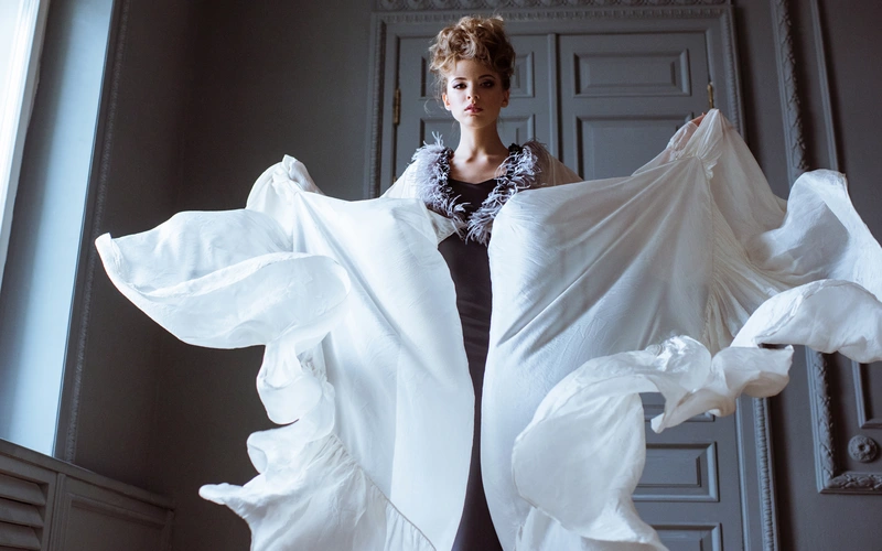 Woman wrapped in flowing white fabric against a dark doorway, an example of artistic fashion photography