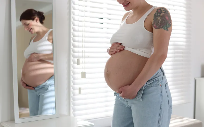 Boudoir maternity picture of a woman holding her belly in front of the mirror