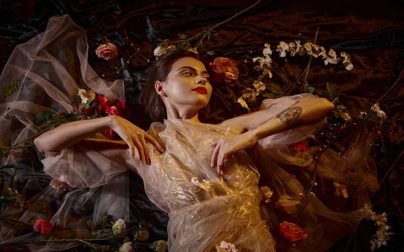 Woman reclining in an ornate gold and floral gown, styled to evoke a classical painting