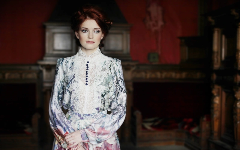 Woman in a floral patterned dress standing in a dimly lit red room with strong directional lighting