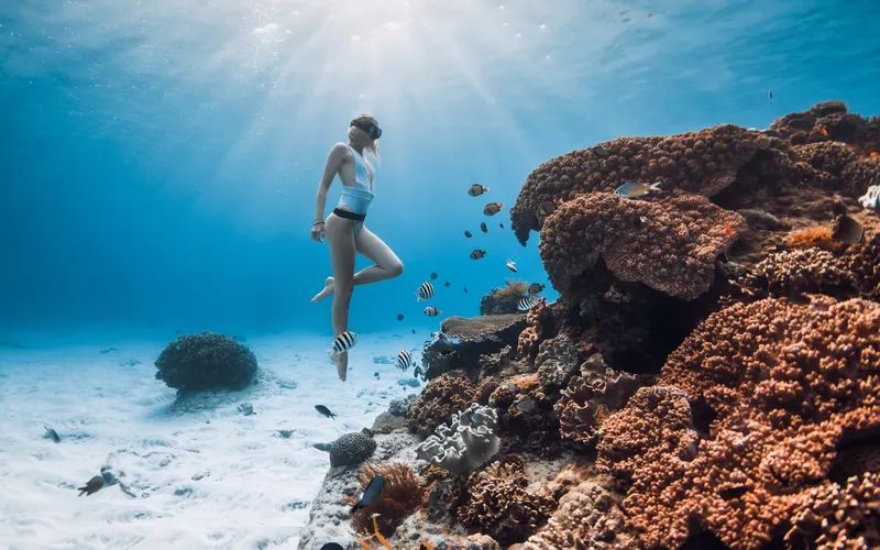 Model posing near coral for a vibrant underwater boudoir photography scene