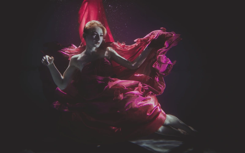 Woman wrapped in pink and magenta fabric, backlit against a dark background for an ethereal glow