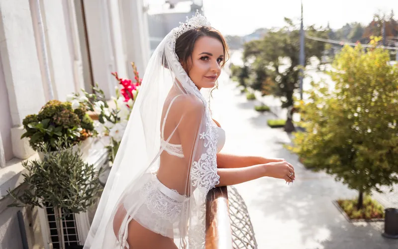 bridal Boudoir photography of a woman in white lingerie and a veil standing on a balcony