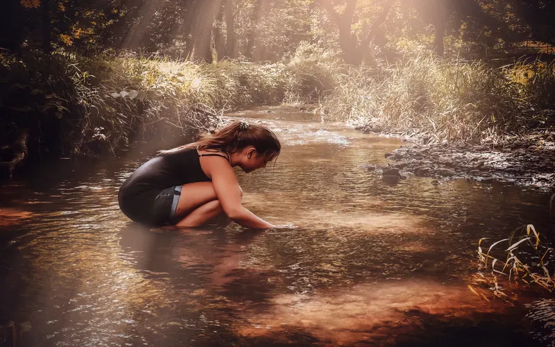 Model standing in a shallow river for creative posing in nature.