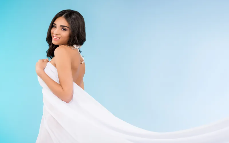 Wedding boudoir portrait of a bride draped in a white fabric in studio