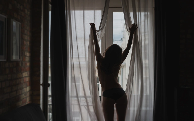 silhouette photo of a woman stretching her arms in front of a window