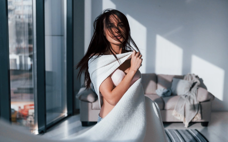 woman with black hair draped around in a white towel in a cozy home