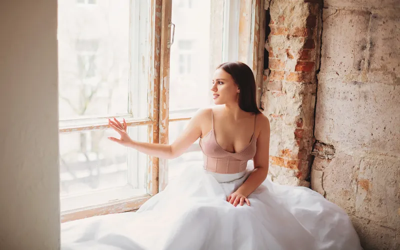 Boudoir bridal photo of a bride in a flowing gown seated by a large window