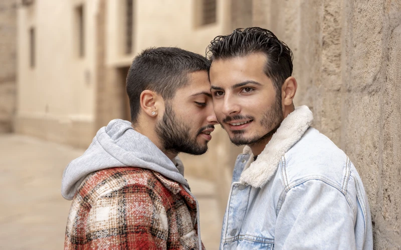 Gay couple standing close with foreheads touching against a stone wall, a candid moment from a gay portrait photography session