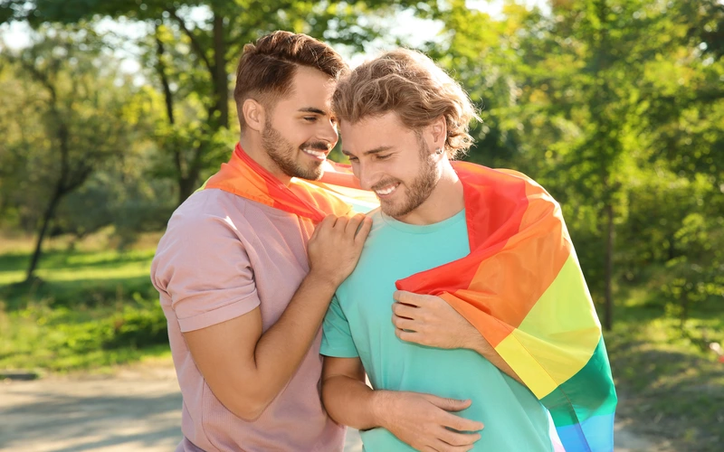 Gay couple with foreheads touching, smiling, framed against soft pride-colored tones