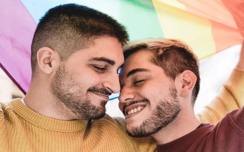 Close-up profile shot of a person at a pride event with a rainbow flag in the background