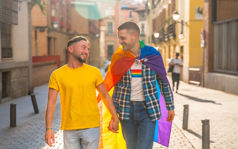 Gay couple walking together with a rainbow flag draped around their shoulders