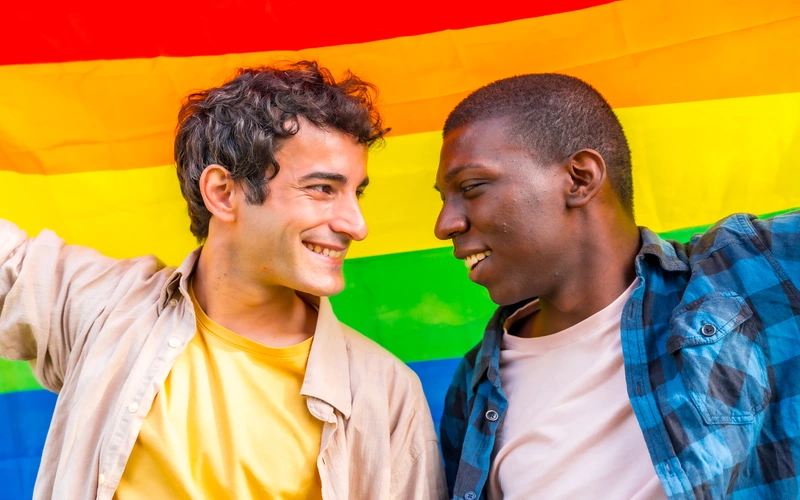 Gay couple laughing together against a bright rainbow pride flag background