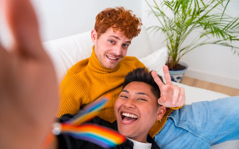 Couple taking a playful selfie-style photo together with a small pride flag