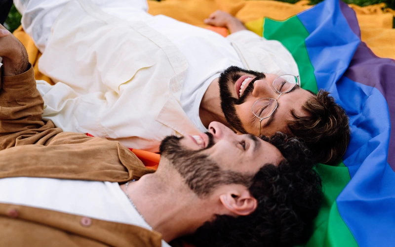 Gay couple lying close together with a rainbow pride flag beneath them, an example of gay photography