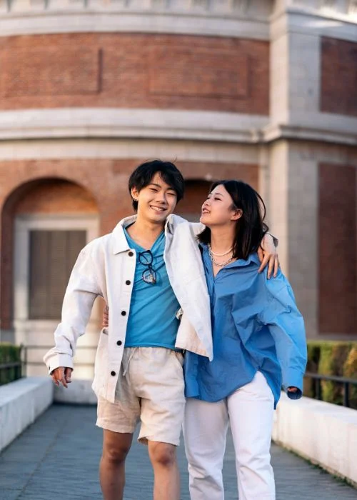 Couple walking arm in arm along a stone bridge near a historic brick building