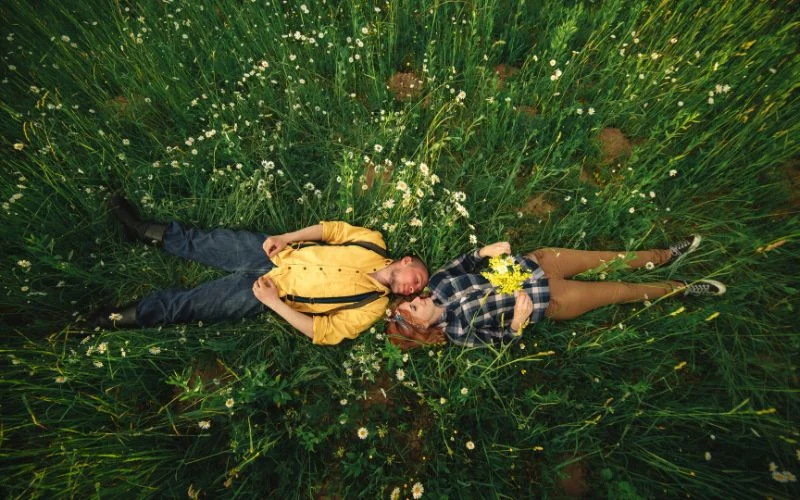 Aerial shot of a couple lying together in a grassy field, arms around each other