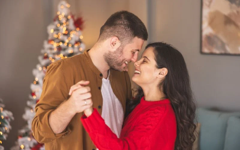 Romantic couple pose of partners dancing close together indoors near a Christmas tree