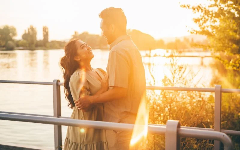 Couple silhouetted against a golden sunset by the water in a romantic embrace