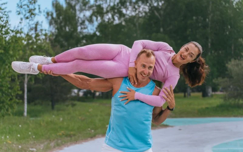 Man joyfully lifting his partner off her feet in a sunny park, both laughing