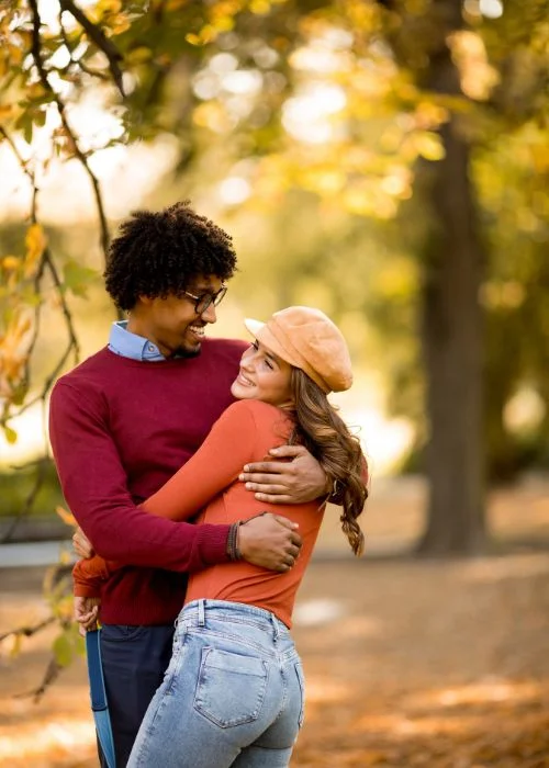 Couple hugging closely on a wooded path surrounded by autumn leaves