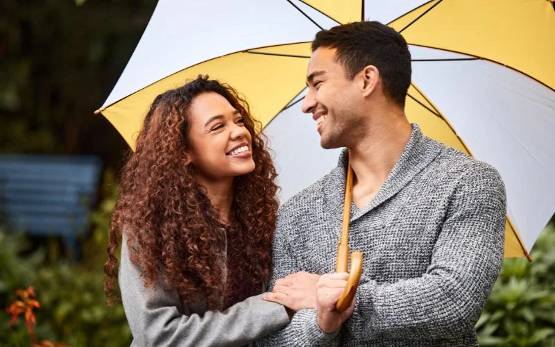 Candid couple pose of a smiling pair sheltering under a yellow umbrella in a park