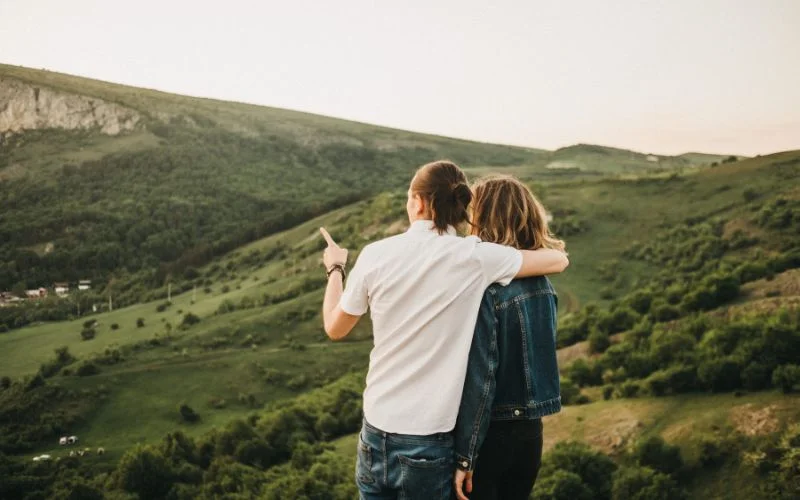 Cute couple pose of partners pointing at a distant view from a green hillside